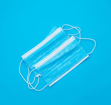 blue sterile medical mask with white elastic bands for doctors on a light blue background, flat lay