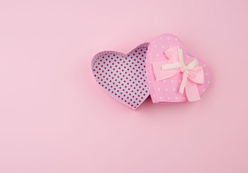 open pink gift box in the form of a heart with a bow on a pink background, top view, festive backdrop