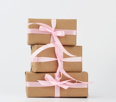 stack of gifts in boxes wrapped in brown kraft paper and tied with silk ribbon on a white background. Festive concept, copy space