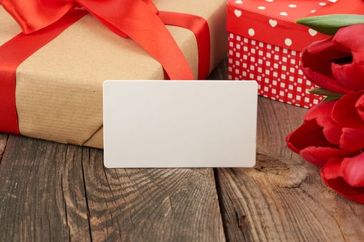 empty rectangular white paper business card, a bouquet of red tulips and wrapped gifts on a gray wooden table. Festive backdrop for birthday, Valentine's day, anniversary