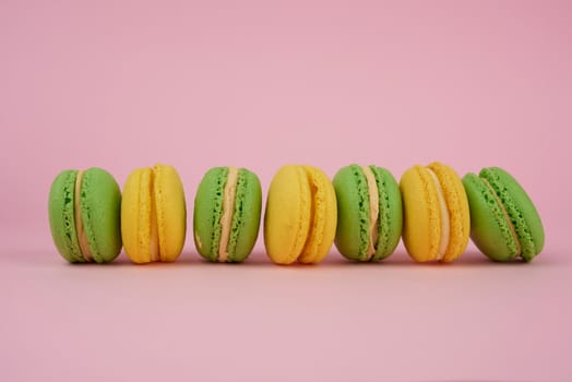 green and yellow round baked macarons on a pink background, delicious popular french dessert
