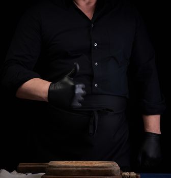 male cook in black uniform and black latex gloves shows like approval gesture, black background