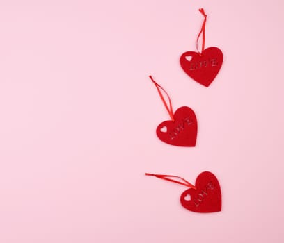 three felt red hearts on a pink background. Holiday celebration concept.