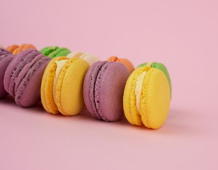 yellow, purple round baked macarons cakes on a pink background, dessert lies in a row, close up