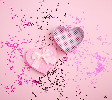 open pink heart-shaped cardboard box on a pink background with multi-colored shiny confetti, festive backdrop for birthday, Valentine's day
