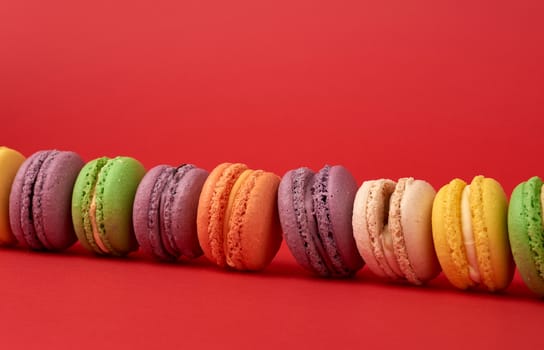 pile of multi-colored baked macarons almond flour cakes on a red background, close up