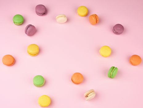 many multi-colored round baked macarons cakes on a light pink background, top view