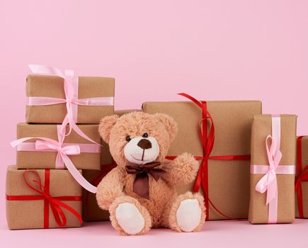 brown cute teddy bear and gifts wrapped in brown eco kraft paper and tied with a ribbon on a pink background, festive backdrop for Valentine's day, birthday