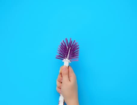 hand holds a plastic brush for cleaning housework, blue background, close up