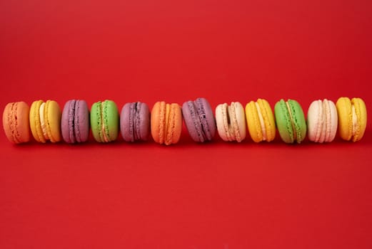 pile of multi-colored baked macarons almond flour cakes on a red background, copy space