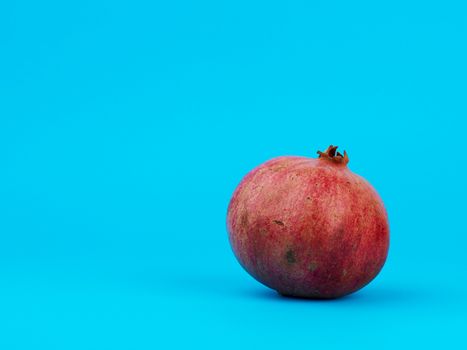 ripe red pomegranate in a peel on a blue background, copy space