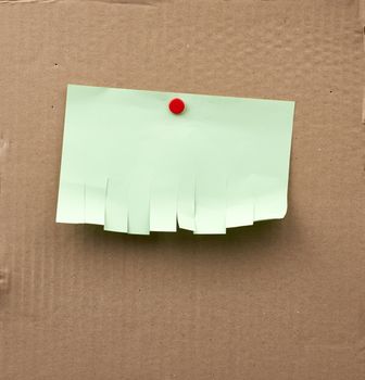 blank paper green ad with torn edges attached with iron buttons on a brown cardboard surface, backdrop for sales and messages