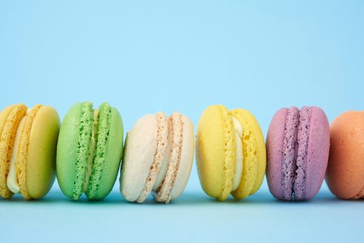 multi-colored round baked macarons cakes on a light blue background, dessert stands in a row, close up
