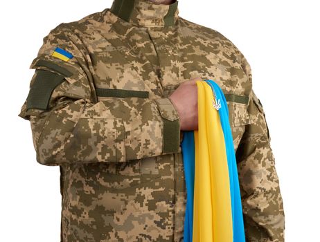 Ukrainian man warrior dressed in a military pixel uniform holds the yellow-blue flag of the state of Ukraine and on the chain a small coat of arms of the country of trident, close up