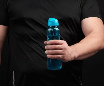 adult male athlete with muscles holds a plastic bottle of water, concept of drinking water in sports and fitness, black background. Lifestyle concept.