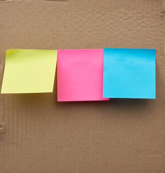blank square multicolored sheets of paper stickers glued on a brown cardboard surface