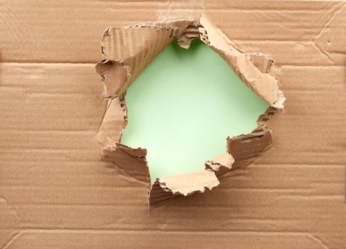 hole in brown cardboard paper with torn and curved edges. Blank template. Green backdrop 