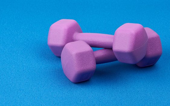 pair of purple plastic dumbbell for sports blue mat, close up. Fitness training. Healthy lifestyle 