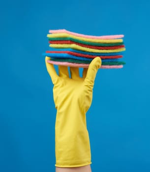 yellow rubber glove for cleaning is put on his hand, part of the body is lifted up and holds a stack of kitchen sponges on a blue background