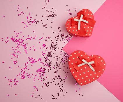 closed red heart-shaped cardboard box on a pink background with multi-colored shiny confetti, festive backdrop for birthday, Valentine's day