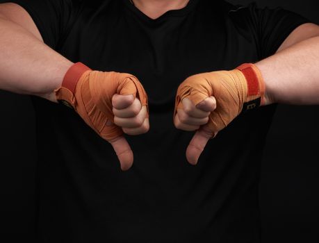 adult athlete in black uniform and hands rewound with textile orange bandage shows gesture dislike, low key