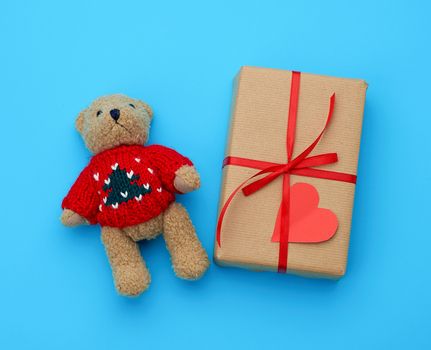 brown gift box and little brown teddy bear on a blue background, top view
