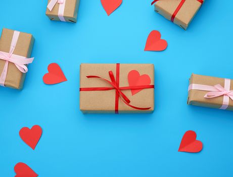 box is wrapped in brown paper and tied with a red thin silk ribbon on a blue background, red cut out paper hearts, copy space, holiday is Valentine's Day