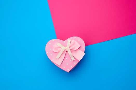 pink gift box in the form of a heart with a bow on a blue background, top view, festive backdrop