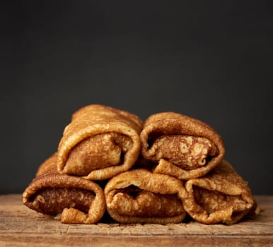 twisted thin fried pancakes with filling lie in a stack on a wooden board, black background