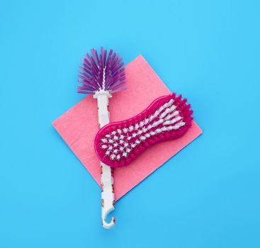 plastic pink brush and square dishwashing rag on a blue background, top view, flat lay
