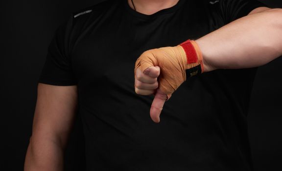 adult athlete in black uniform and hands rewound with textile orange bandage shows gesture dislike, low key