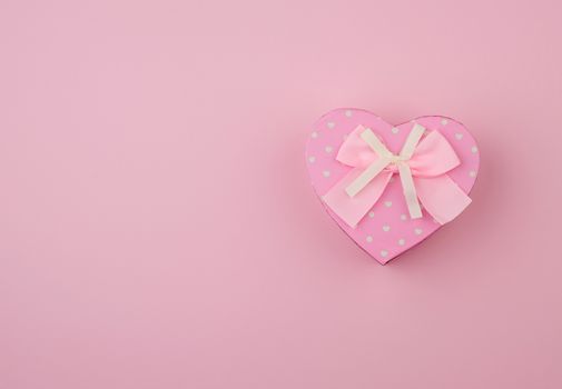 pink gift box in the form of a heart with a bow on a pink background, top view, festive backdrop
