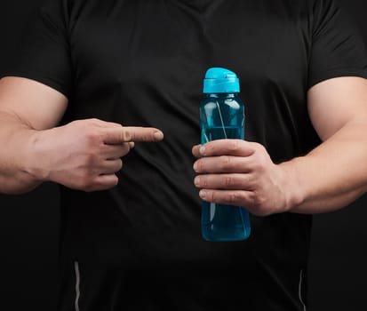 adult male athlete with muscles holds a plastic bottle of water, concept of drinking water in sports and fitness, black background