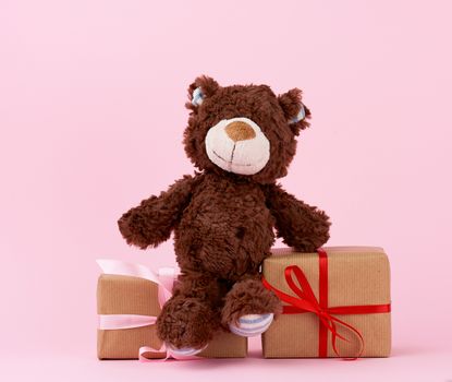 brown cute teddy bear and gifts wrapped in brown eco kraft paper and tied with a ribbon on a pink background, festive backdrop for Valentine's day, birthday