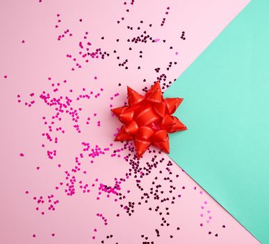 red bow and shiny multicolored round confetti scattered on a pink-green abstract background, festive backdrop for birthday, valentines day
