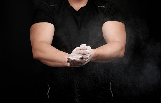 muscular athlete in a black uniform rubs his hands with white dry sports magnesia, powder scatters in different directions on a black background