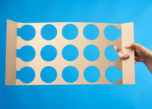 hand holds brown paper partition with round drawer openings, blue background 