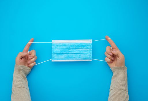 female hands protracted blue sterile textile medical mask with white elastic bands for doctors on a light blue background, flat lay