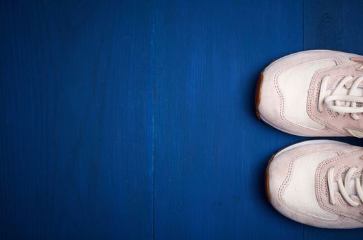 pair of leather pink sneakers on a blue wooden background, top view, copy space
