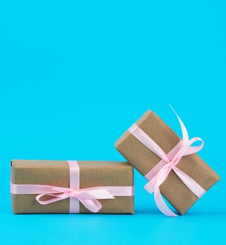 gifts in boxes wrapped in brown kraft paper and tied with pink silk ribbon on a blue background. Festive concept, copy space