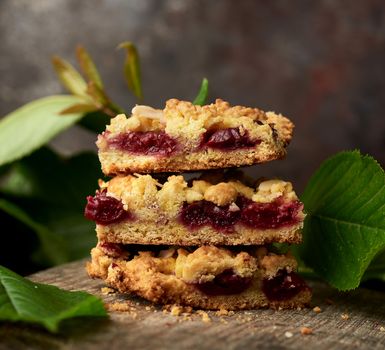 stack of square pieces of crumble pie with cherry on a wooden board, delicious dessert