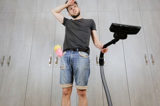 A man with a vacuum cleaner is tired of cleaning the house