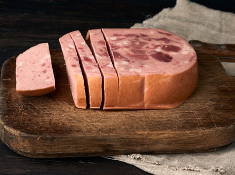 sliced boiled sausage with slices of whole meat on a brown wooden cutting board, close up