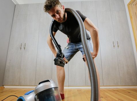 A man with a vacuum cleaner is tired of cleaning the house