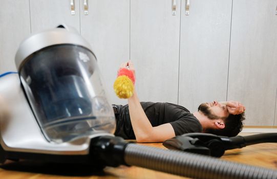 A man with a vacuum cleaner is tired of cleaning the house