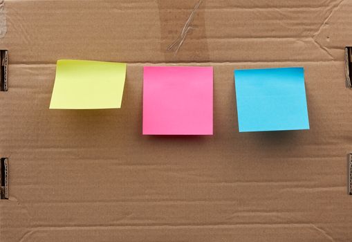 blank pink, yellow and blue square papers  glued on a brown cardboard surface. Design template.