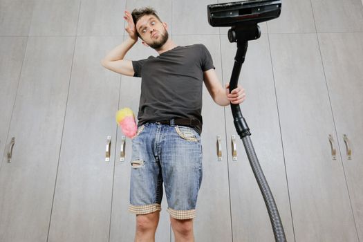 A man with a vacuum cleaner is tired of cleaning the house