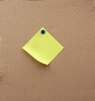 blank square sheet of paper attached with an iron button on a brown cardboard surface. Design template.