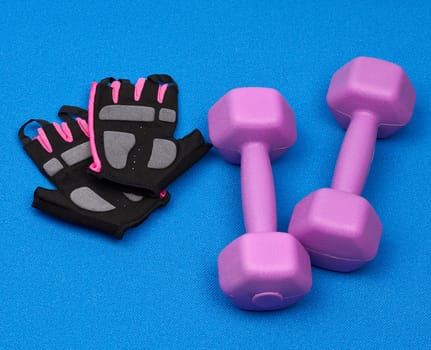 pair of purple plastic dumbbells, gloves on a blue neoprene mat, top view, training equipment