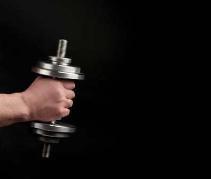 man holds steel dumbbells in his hands, his muscles are tense, low key, sports background, copy space